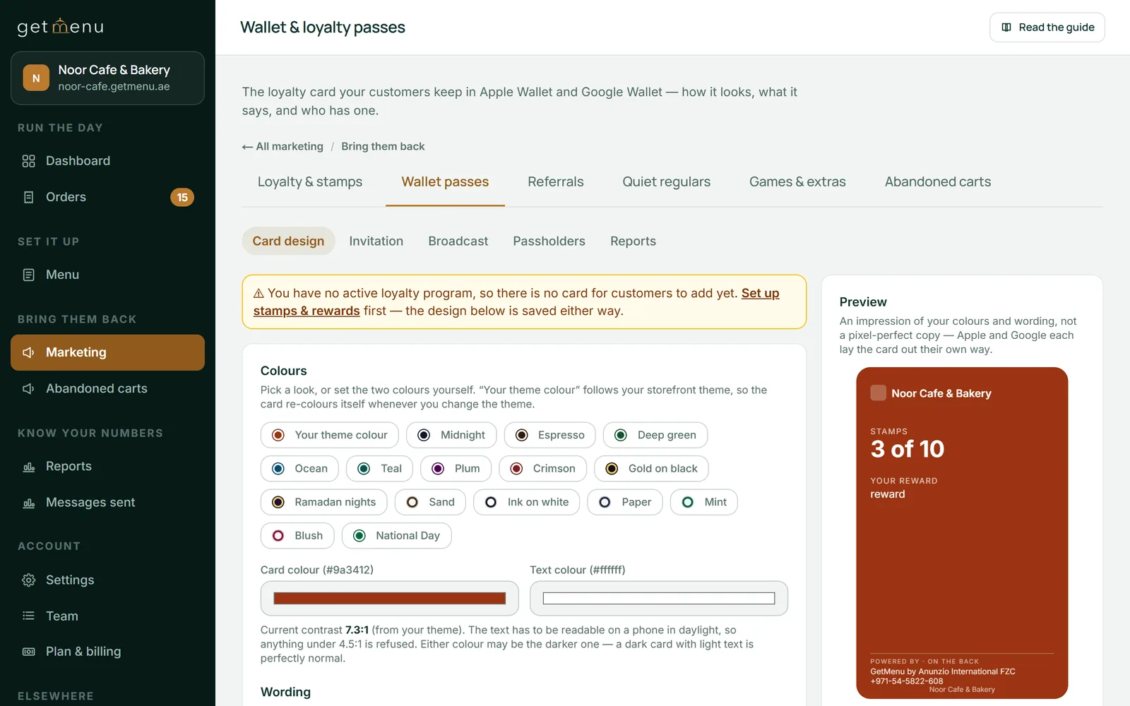 The Wallet passes page of the GetMenu dashboard for Noor Cafe & Bakery, on the Card design tab. A yellow notice says there is no active loyalty program yet, so there is no card for customers to add. Below it are colour themes such as Midnight, Espresso, Ocean and National Day, the card and text colours with a contrast of 7.3 to 1, and on the right a red preview card reading Noor Cafe & Bakery, Stamps 3 of 10.